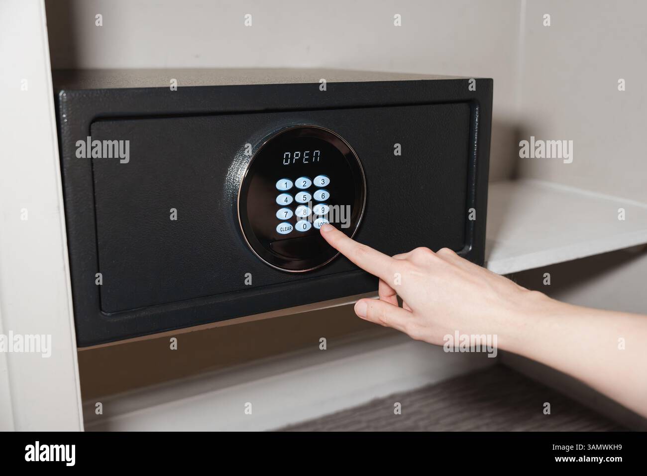 Eine Person gibt über die Tastatur einen Code in einem digitalen Hotelsafe ein, auf dem das Wort GEÖFFNET angezeigt wird Stockfoto