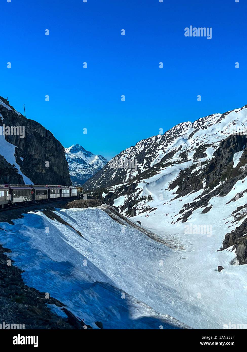 Eine atemberaubende Zugfahrt durch einen schneebedeckten Bergpass in Alaska. Die White Pass & Yukon Route Railroad schlängelt sich durch das raue Gelände - Smartphone-aufgenommenes Stockfoto