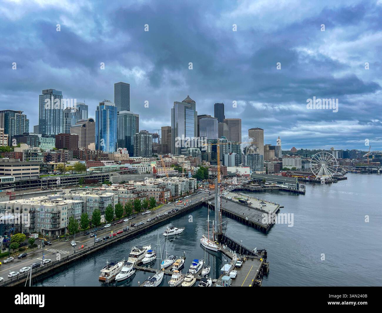 Ein atemberaubender Blick auf die Küste von Seattle mit der berühmten Skyline der Stadt, dem geschäftigen Yachthafen und dem Seattle Great Wheel. Der bewölkte Himmel fügt hinzu - Smartphone-aufgenommenes Stockfoto