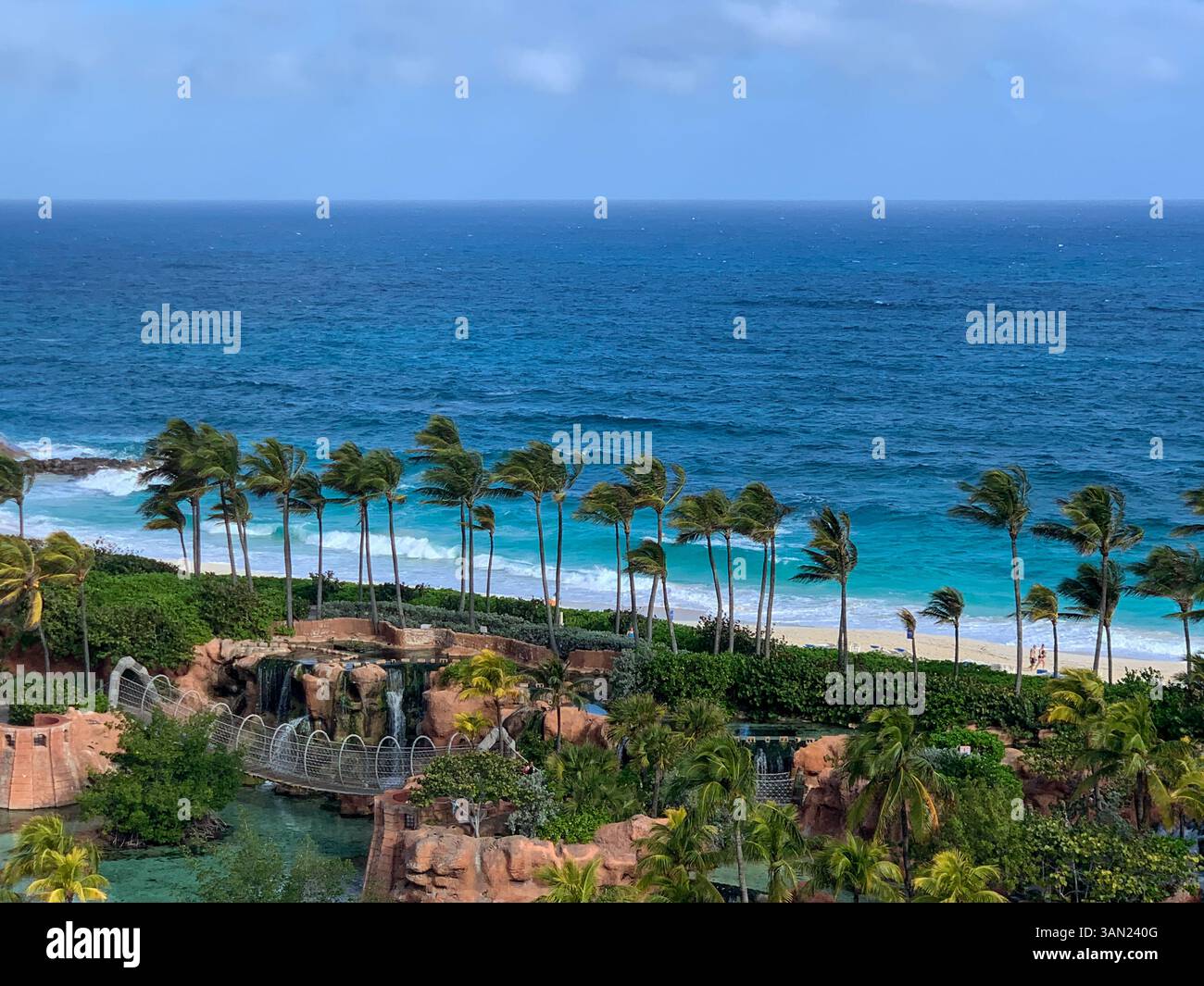 Ein atemberaubender Blick auf ein tropisches Paradies mit sich wiegenden Palmen, türkisfarbenen Meereswellen und einem luxuriösen Strandresort. Der perfekte Zufluchtsort - Smartphone-aufgenommenes Stockfoto