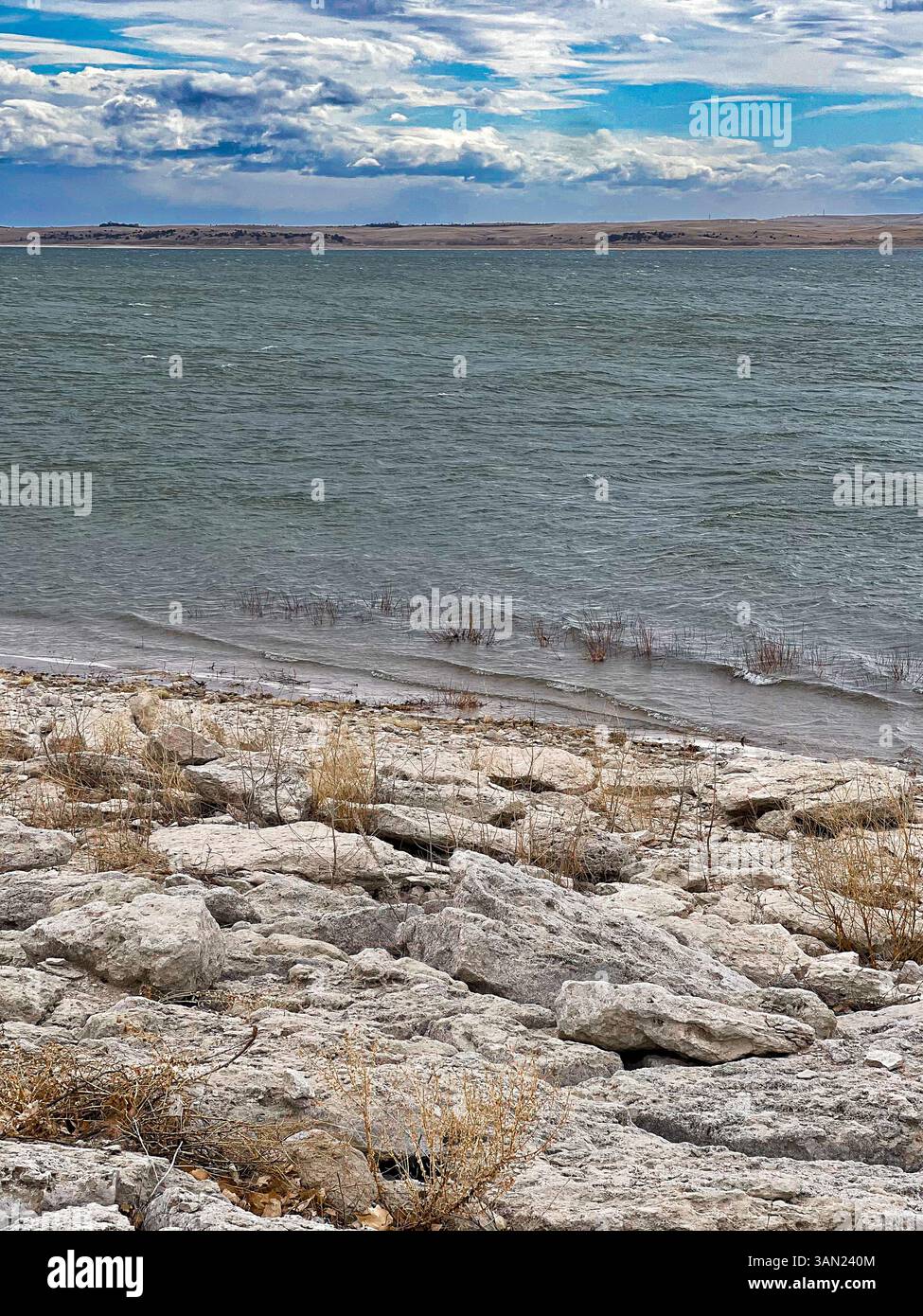 Die Wellen wallen über den See, während der Wind unter einem brodelnden Himmel durch die felsige Küste zieht und die raue Schönheit des ruhigen Dramas der Natur einfängt. - Smartphone-aufgenommenes Stockfoto