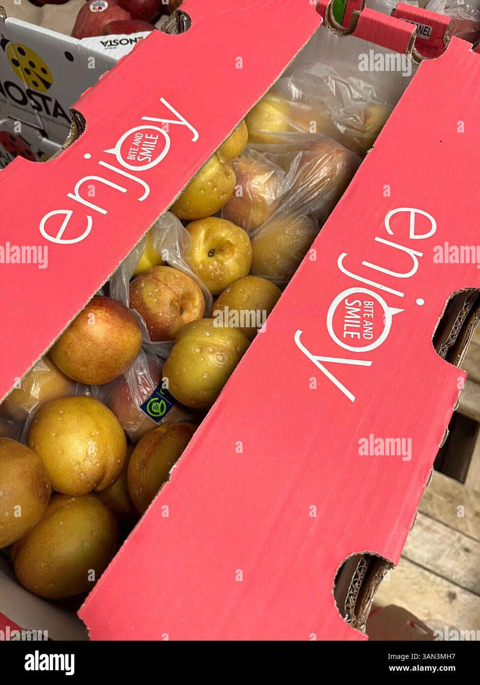 Frische reife Nektarinen in rosafarbener Pappkiste mit der Aufschrift „Enjoy“, vertriebsfertig, Großhandel, Obstmarkt, Vertrieb, Lebensmittelversorgung, rosafarbene Kiste - Smartphone-aufgenommenes Stockfoto