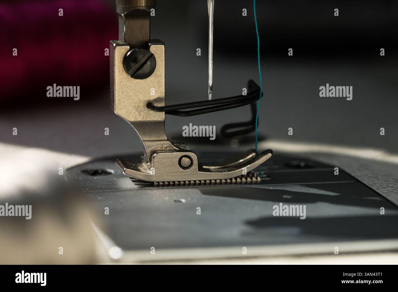Nahaufnahme der Nadel und des Nähfußes der industriellen Nähmaschine mit natürlichem Tageslicht. Kreatives Konzept der Details von Nähgeräten Stockfoto