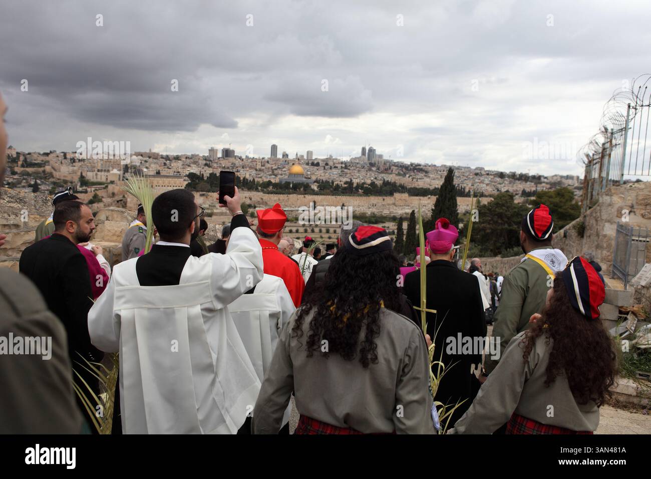 Christliche Pilger gehen vom Mt. Oliven in einer Palmensonntagsprozession mit Palmenwedel und Olivenbaumzweigen die Kuppel des Felsens gesehen. Stockfoto