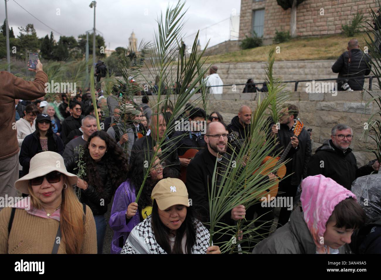 Christliche Pilger in der ganzen Welt singen und beten, während sie auf dem Mt. Oliven in einer Palmensonntagsprozession mit Palmenwedel und Olivenbaumzweigen. Stockfoto
