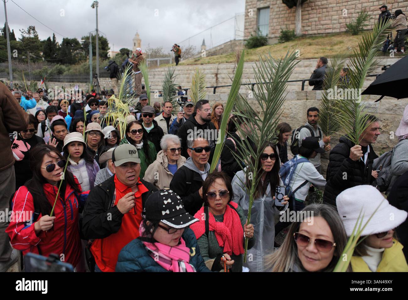 Christliche Pilger in der ganzen Welt singen und beten, während sie auf dem Mt. Oliven in einer Palmensonntagsprozession mit Palmenwedel und Olivenbaumzweigen. Stockfoto