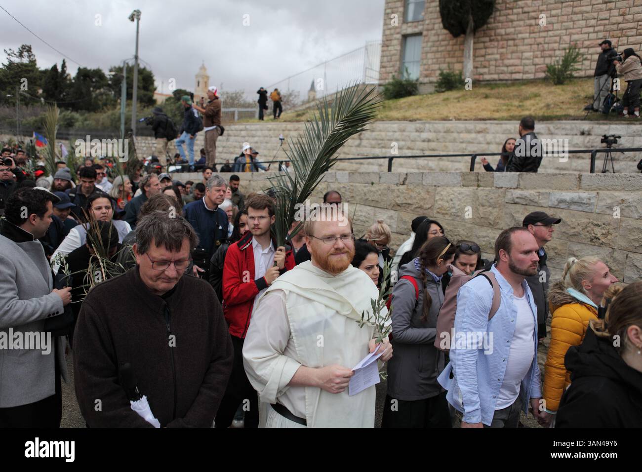 Christliche Pilger in der ganzen Welt singen und beten, während sie auf dem Mt. Oliven in einer Palmensonntagsprozession mit Palmenwedel und Olivenbaumzweigen. Stockfoto