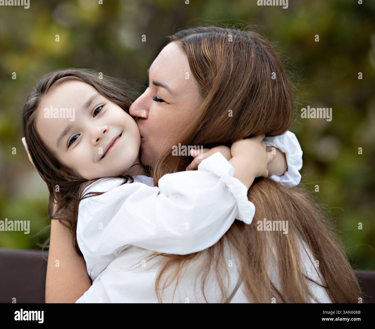 Tochter umarmt Mutter, Mama küsst Tochter. Sie lächeln warm, während sie ihre Gesichter dicht aneinander lehnen und Glück und Liebe ausstrahlen. Stockfoto