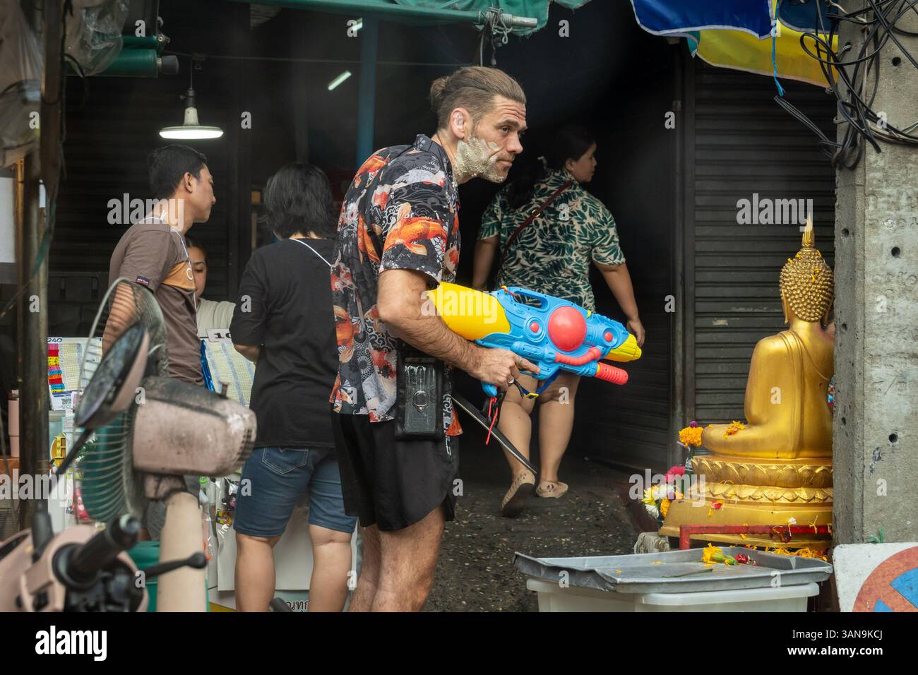 Bangkok, Thailand. April 2025. Ein Ausländer, der mit einer Wasserpistole in der Nähe einer goldenen buddhistischen Statue während des Songkran Festivals auf dem Huai Khwang Markt gesehen wurde. Songkran, Thailands traditionelles Neujahrsfest, das ab April 13-15 stattfindet, ist eine der lebhaftesten und freudigsten Feierlichkeiten des Landes. Die Stadt ist vor allem für ihre massiven Wasserkämpfe auf den Straßen bekannt, die das Abwaschen von Unglück und Unglück symbolisieren und einen Neuanfang für das kommende Jahr darstellen. Quelle: SOPA Images Limited/Alamy Live News Stockfoto