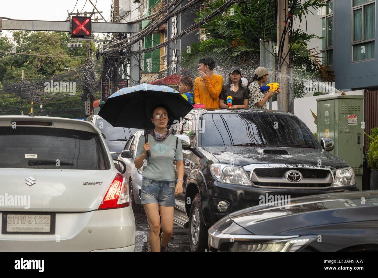 Bangkok, Thailand. April 2025. Während des Songkran Festivals auf dem Huai Khwang Market hält eine Frau mitten im Verkehr einen Schirm. Songkran, Thailands traditionelles Neujahrsfest, das ab April 13-15 stattfindet, ist eine der lebhaftesten und freudigsten Feierlichkeiten des Landes. Die Stadt ist vor allem für ihre massiven Wasserkämpfe auf den Straßen bekannt, die das Abwaschen von Unglück und Unglück symbolisieren und einen Neuanfang für das kommende Jahr darstellen. Quelle: SOPA Images Limited/Alamy Live News Stockfoto