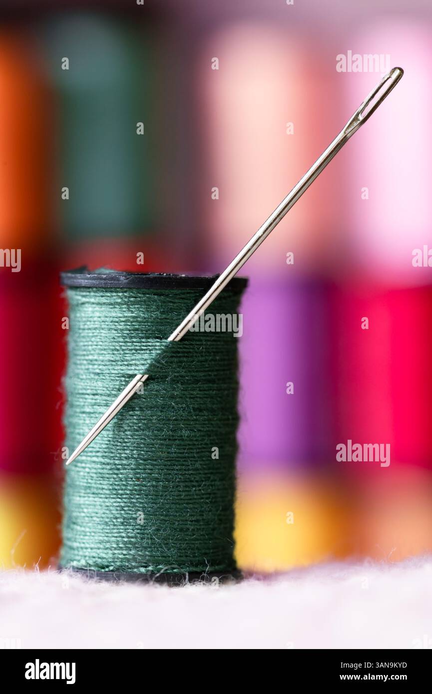 Eine Spule aus grünem Garn mit einer Nähnadel, bunte Spulen im Hintergrund Stockfoto