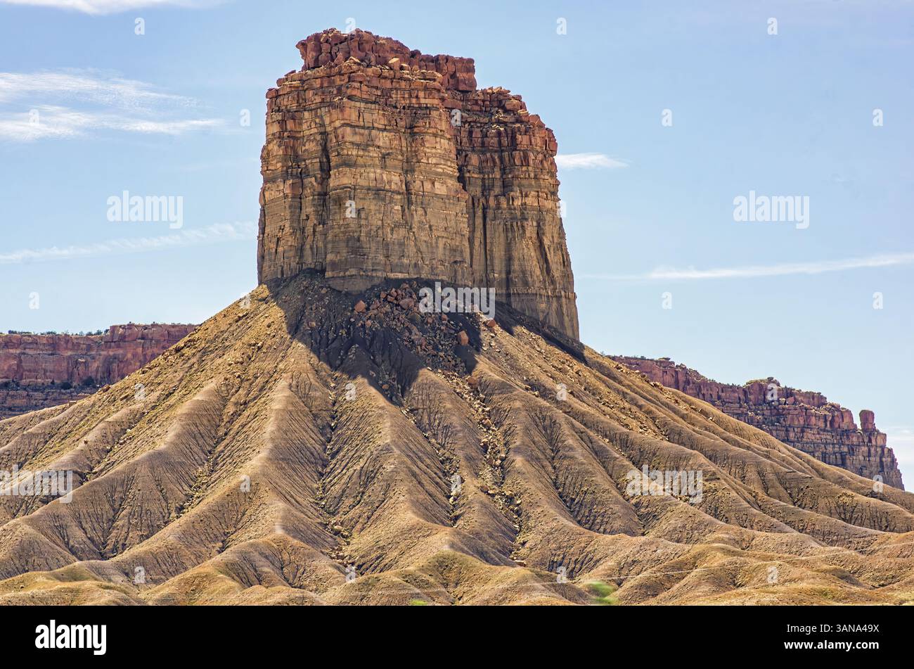 Die markante Wüste butte erhebt sich aus einem Fan erodierter Grate und geschichteter Felsformationen unter einem klaren Himmel im amerikanischen Südwesten. Stockfoto