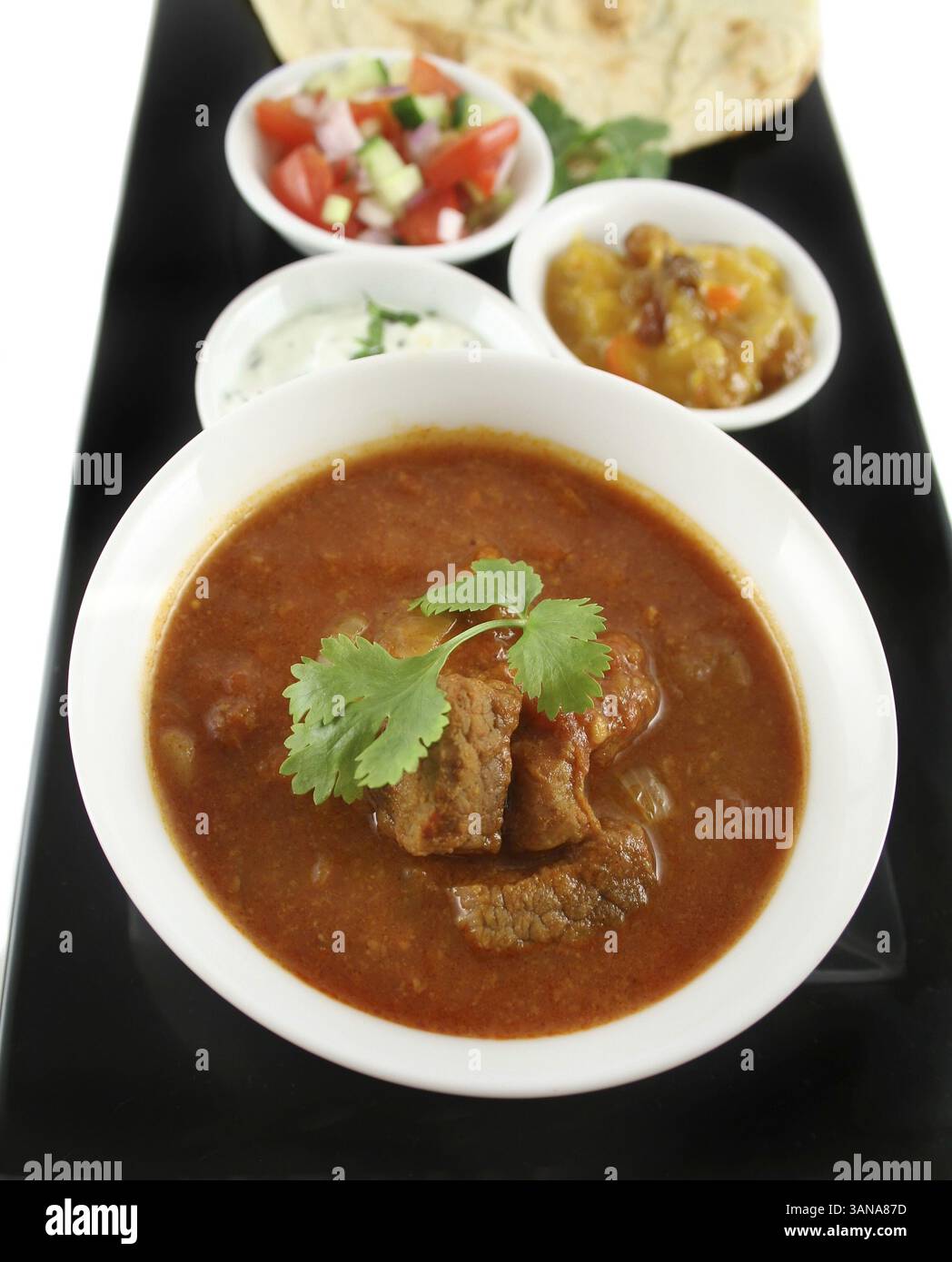 Indisches fest mit Vindaloo-Curry, Naan-Brot, Mango-Chutney, Banane und Kokos, Tomaten und Gurken Stockfoto