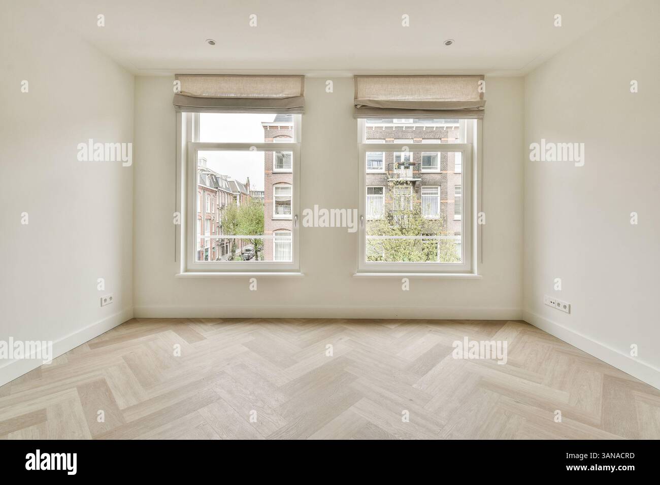 Ein minimalistischer Innenraum mit großen Fenstern, die natürliches Licht einströmen lassen, bietet eine neutrale Farbpalette und Holzfußboden. Stockfoto