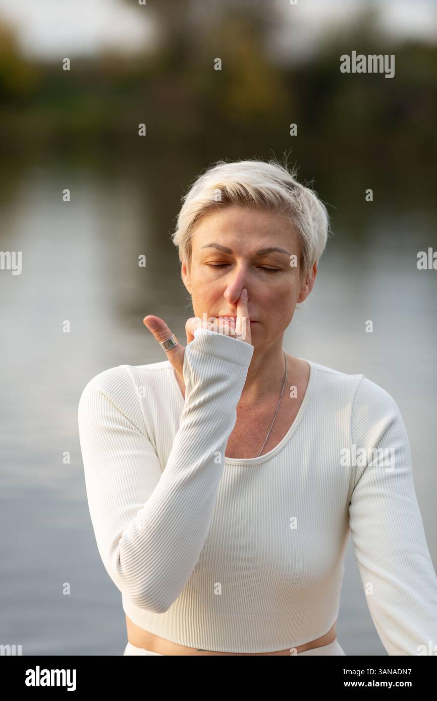 Eine Erwachsene Frau in einem weißen Anzug engagiert sich im Kundalini-Yoga, der Praxis von Nadi-shodhana pranayama Stockfoto