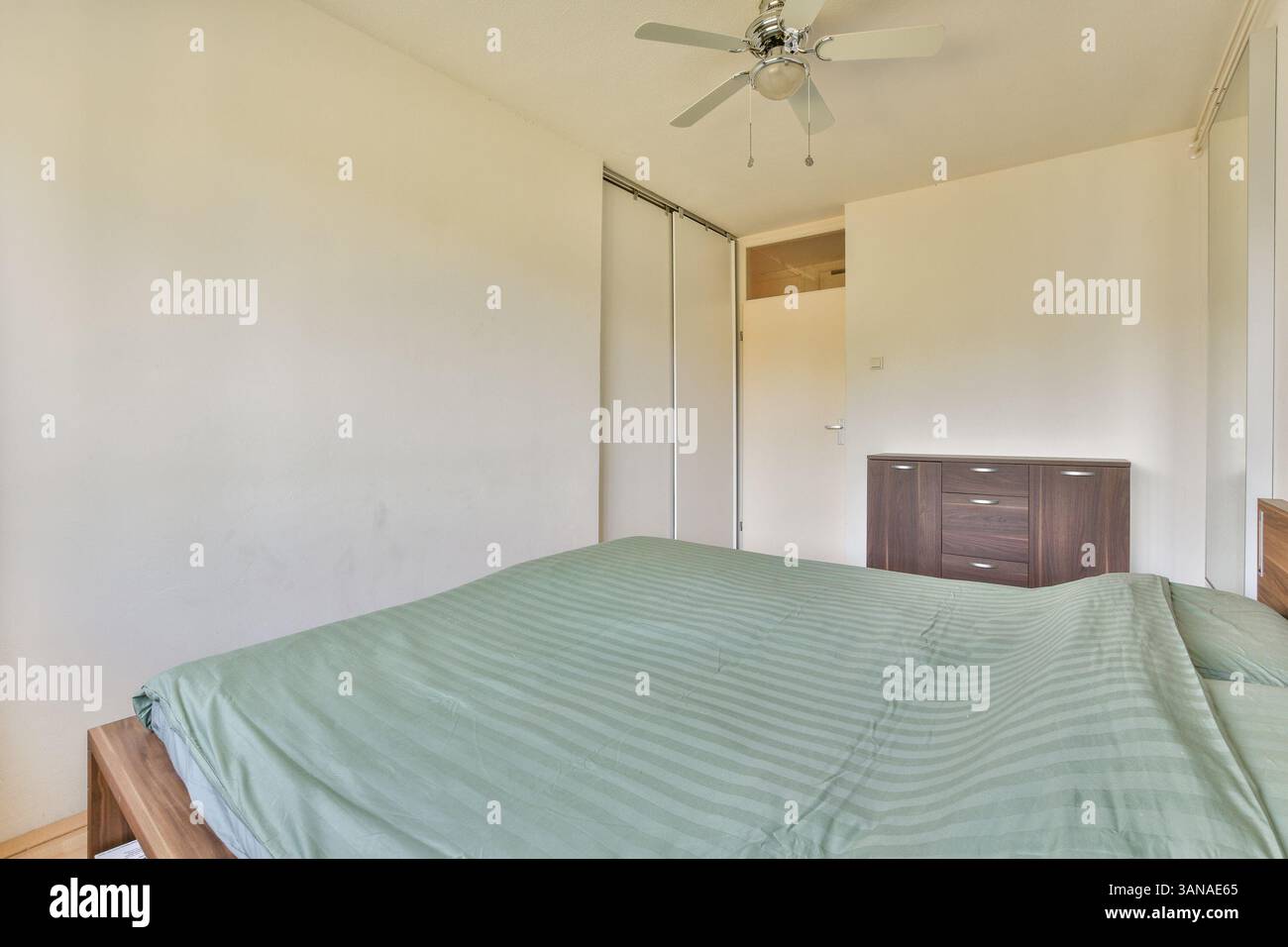 Ein ruhiges Schlafzimmer mit weichgrüner Bettwäsche, neutralen Wänden und Holzakzenten. Tageslicht verstärkt die ruhige Atmosphäre und macht sie einladend und friedlich. Stockfoto