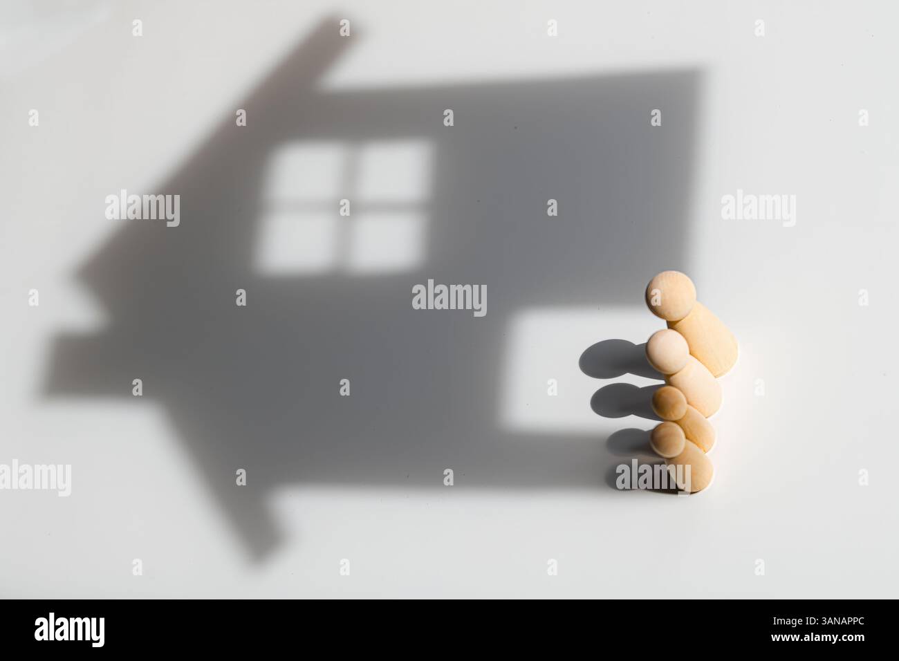 Familie aus Holz, die den Schatten eines Hauses wirft, symbolisiert Familienleben, Wohnungssicherheit, Wohnungsträume, Stabilität, und Zugehörigkeit Stockfoto