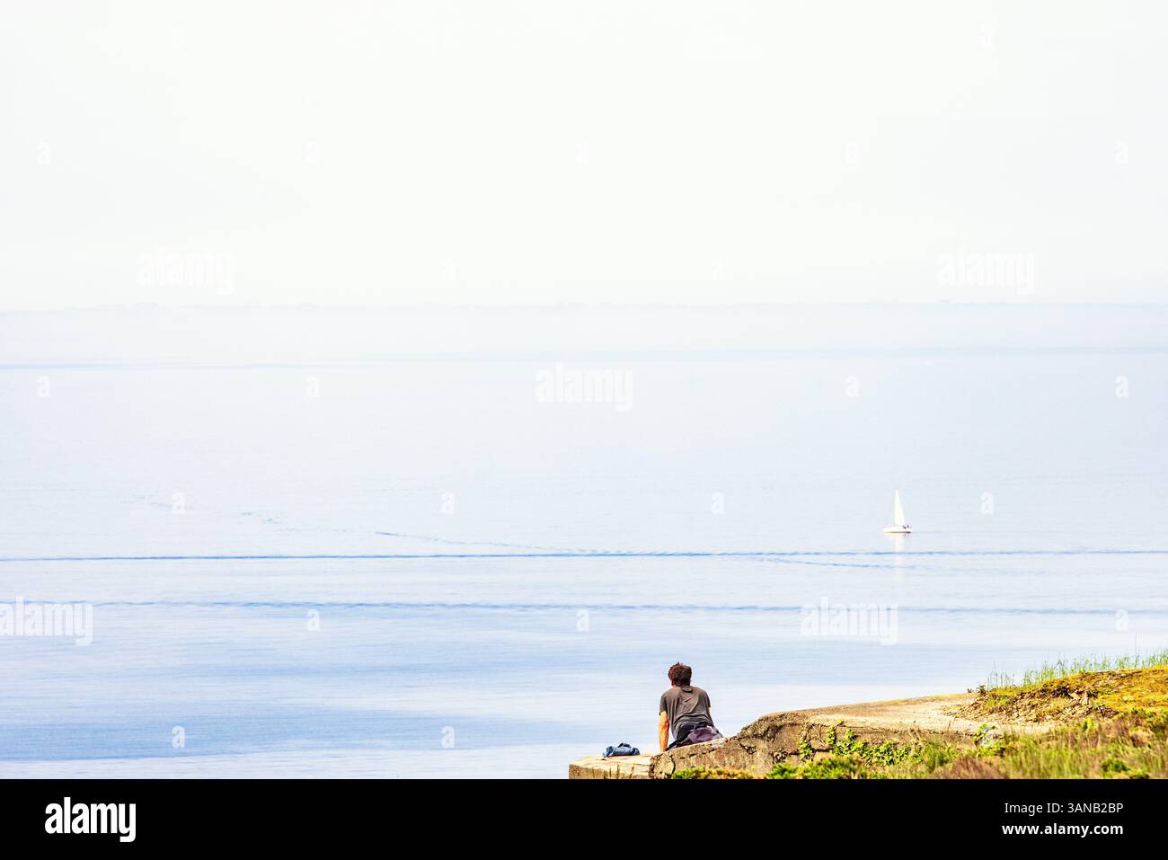 Allein sitzender Mann, der auf das Meer bis zum Horizont blickt Stockfoto