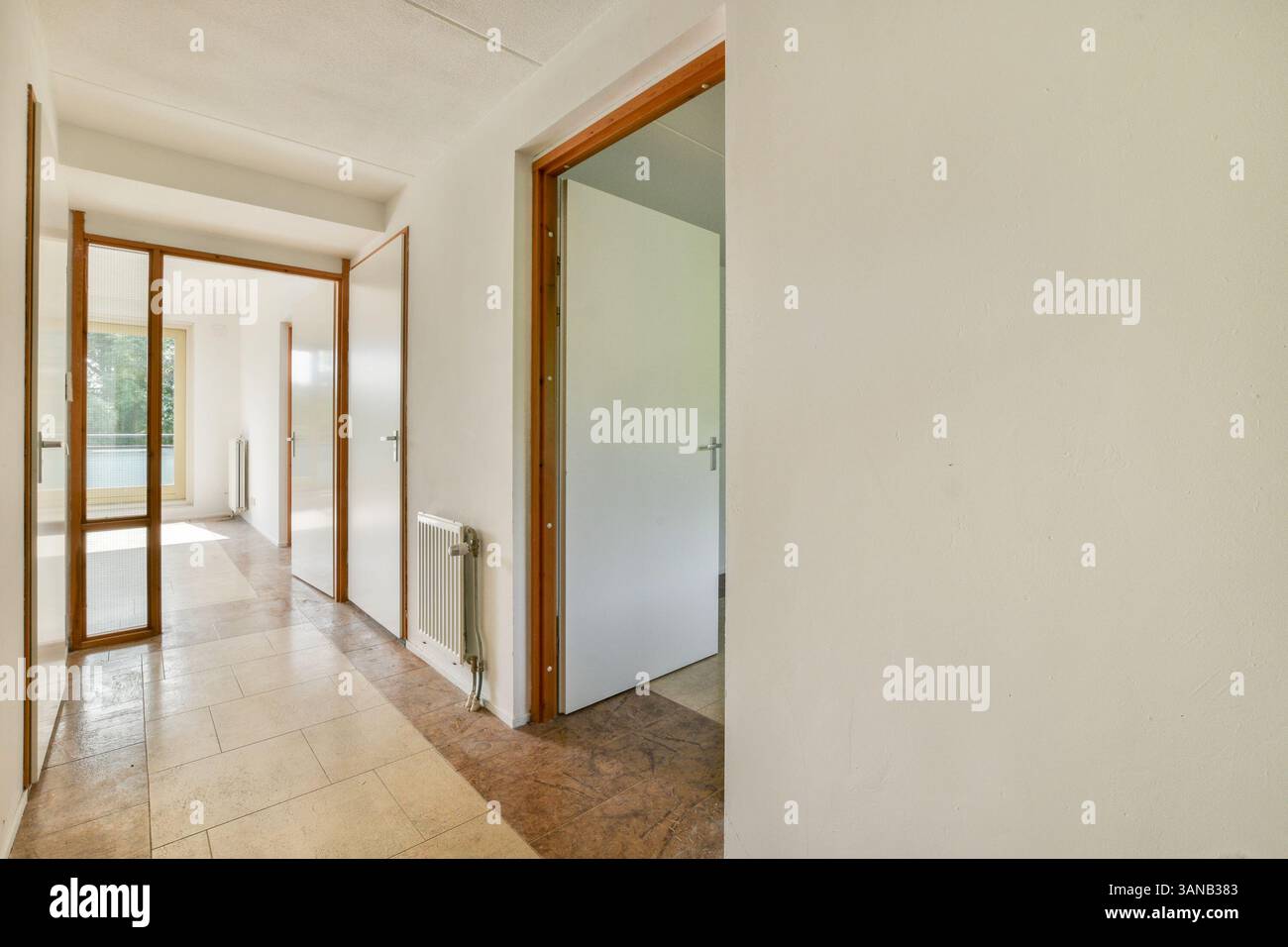 Ein weitläufiger Flur mit hellen Wänden und Holztüren, beleuchtet durch natürliches Licht, schafft ein warmes Ambiente im Raum. Stockfoto