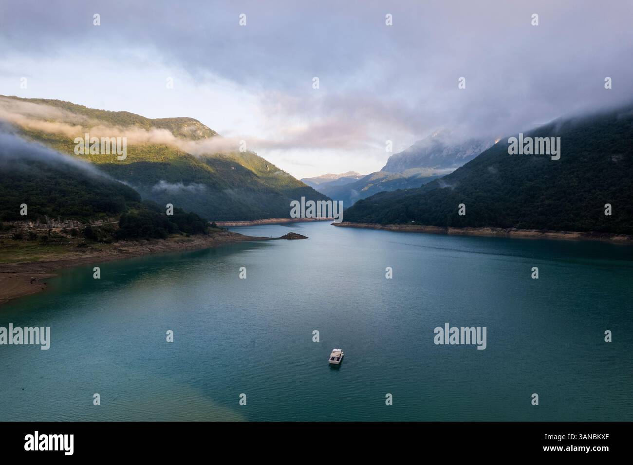 Blick aus der Vogelperspektive auf den Piva-See mit einem kleinen Boot umgeben von ruhigen Bergen und Wolken, Pluzine, Montenegro. Stockfoto