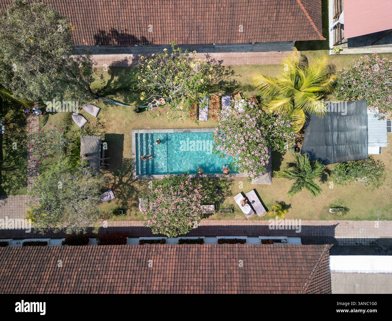 Blick aus der Vogelperspektive auf den luxuriösen Resortpool mit entspannenden Menschen, umgeben von tropischen Gärten und Palmen, Kuta Selatan, Indonesien. Stockfoto