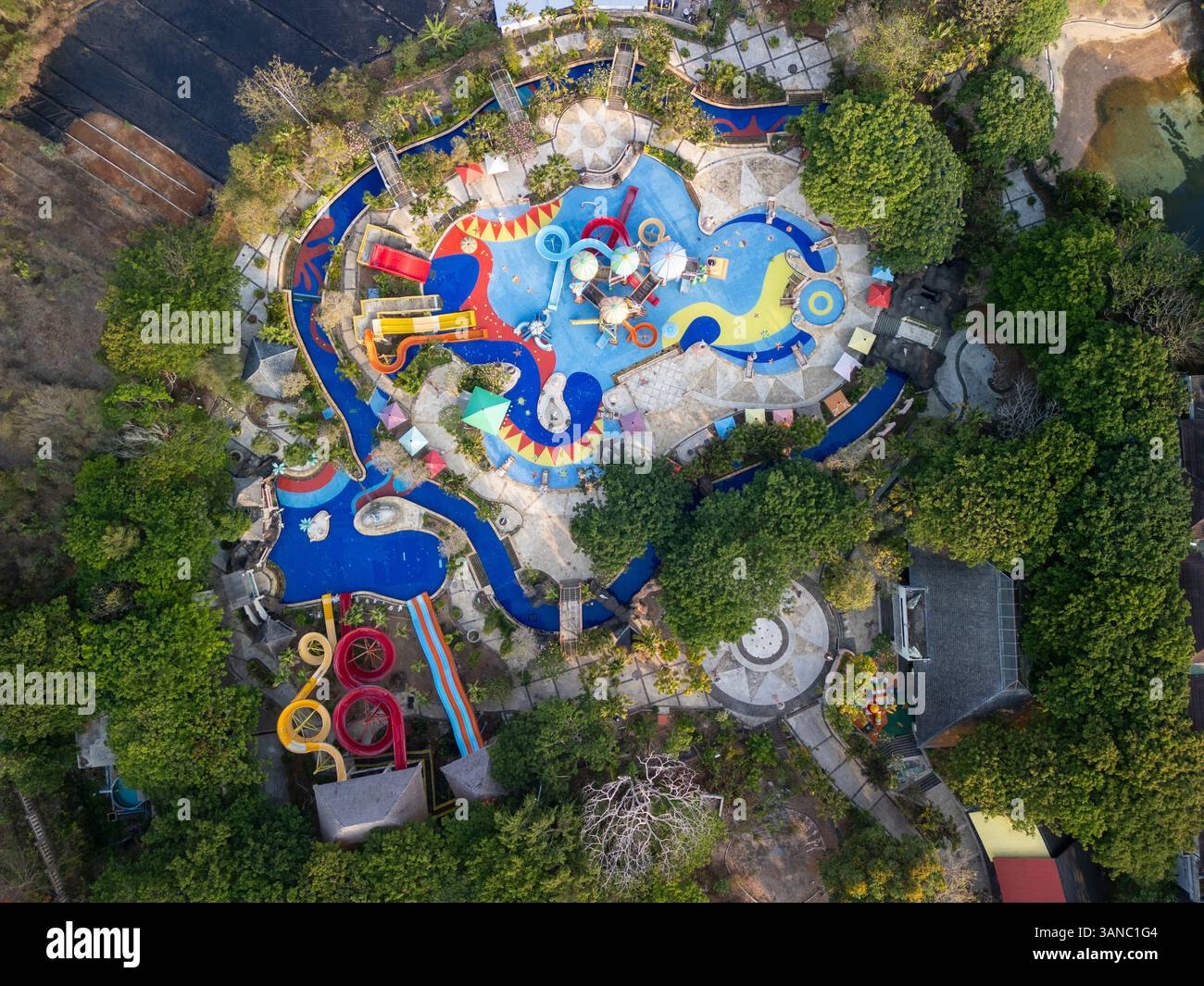 Blick aus der Vogelperspektive auf einen farbenfrohen Wasserpark mit Rutschen und Pools, umgeben von üppigem Grün und Bäumen, Kuta Selatan, Bali, Indonesien. Stockfoto