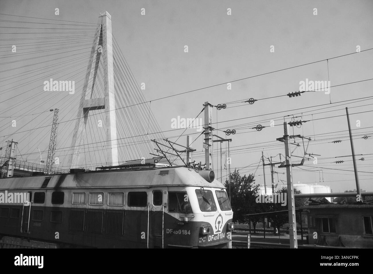 Schwarzweißfoto der DF4-Lokomotive unter der Jinan-Brücke – Industrial Railway Infrastructure and Modern Transportation Stockfoto