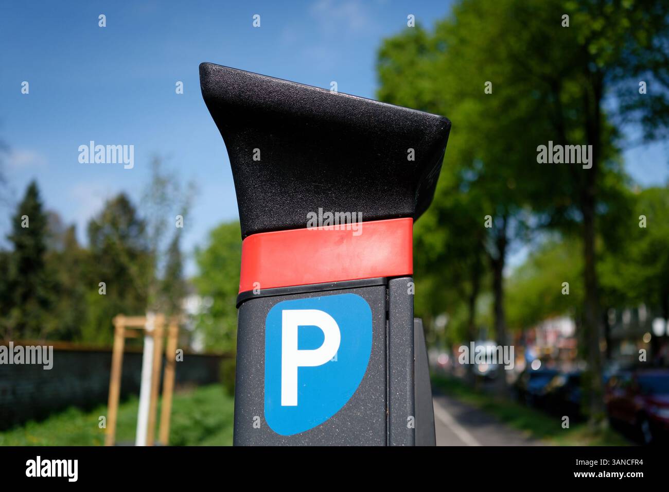 Nahaufnahme einer modernen Parkuhr in einer urbanen Umgebung im Freien in einem Wohngebiet mit Bäumen, geparkten Autos und einem Bürgersteig in verschwommenem Hintergrund Stockfoto