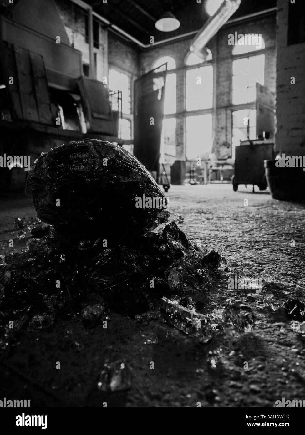 OLYMPUS DIGITAL CAMERAGlasfragmente stapeln sich auf dem Boden einer Vintage-Werkstatt, mit einem verschwommenen Hintergrund von Maschinen und Fenstern. Stockfoto