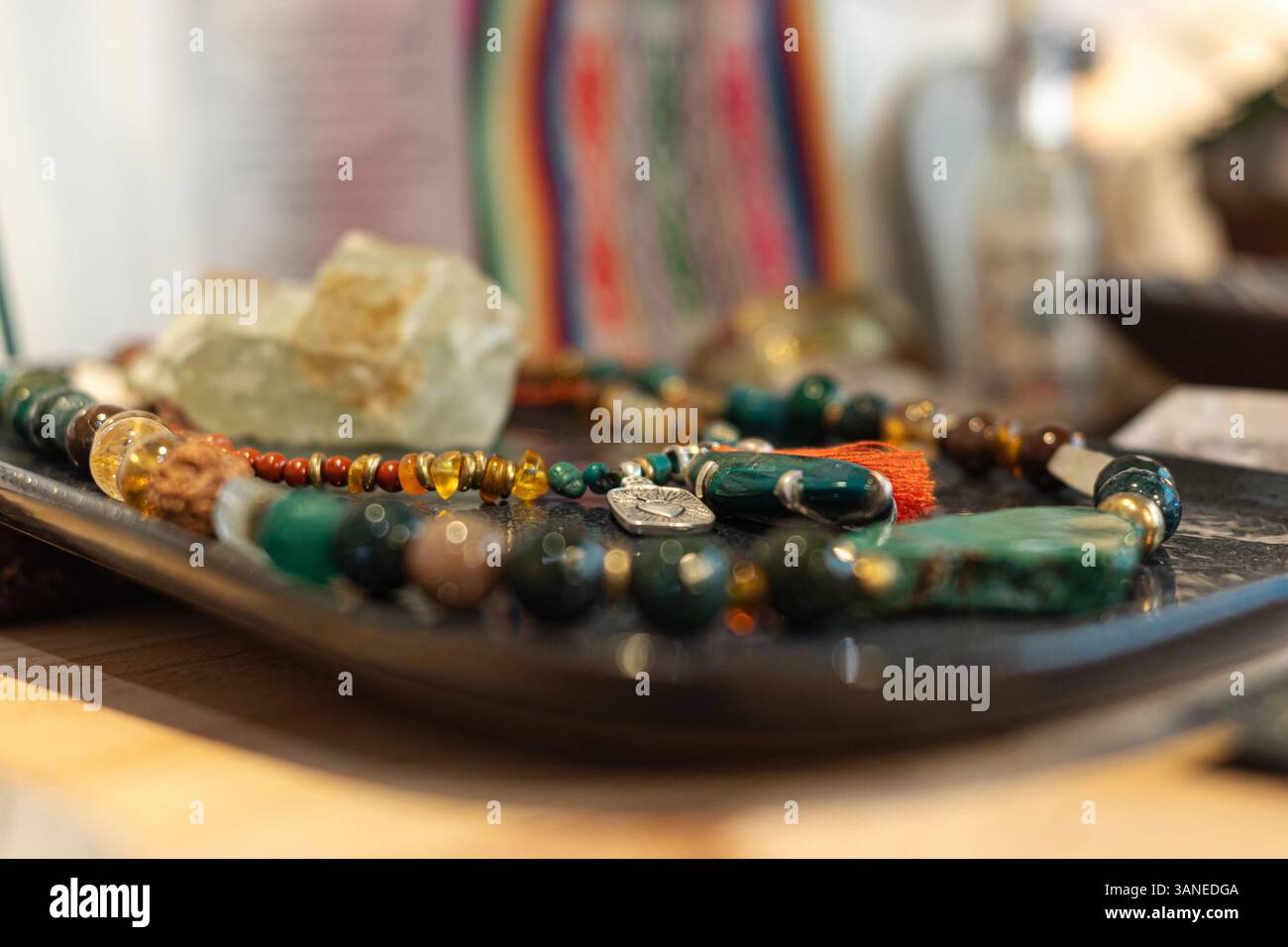 Nahaufnahme einer farbenfrohen Perlenkette und rohen Edelsteinen auf einer dunklen, strukturierten Oberfläche in einer verschwommenen Umgebung Stockfoto