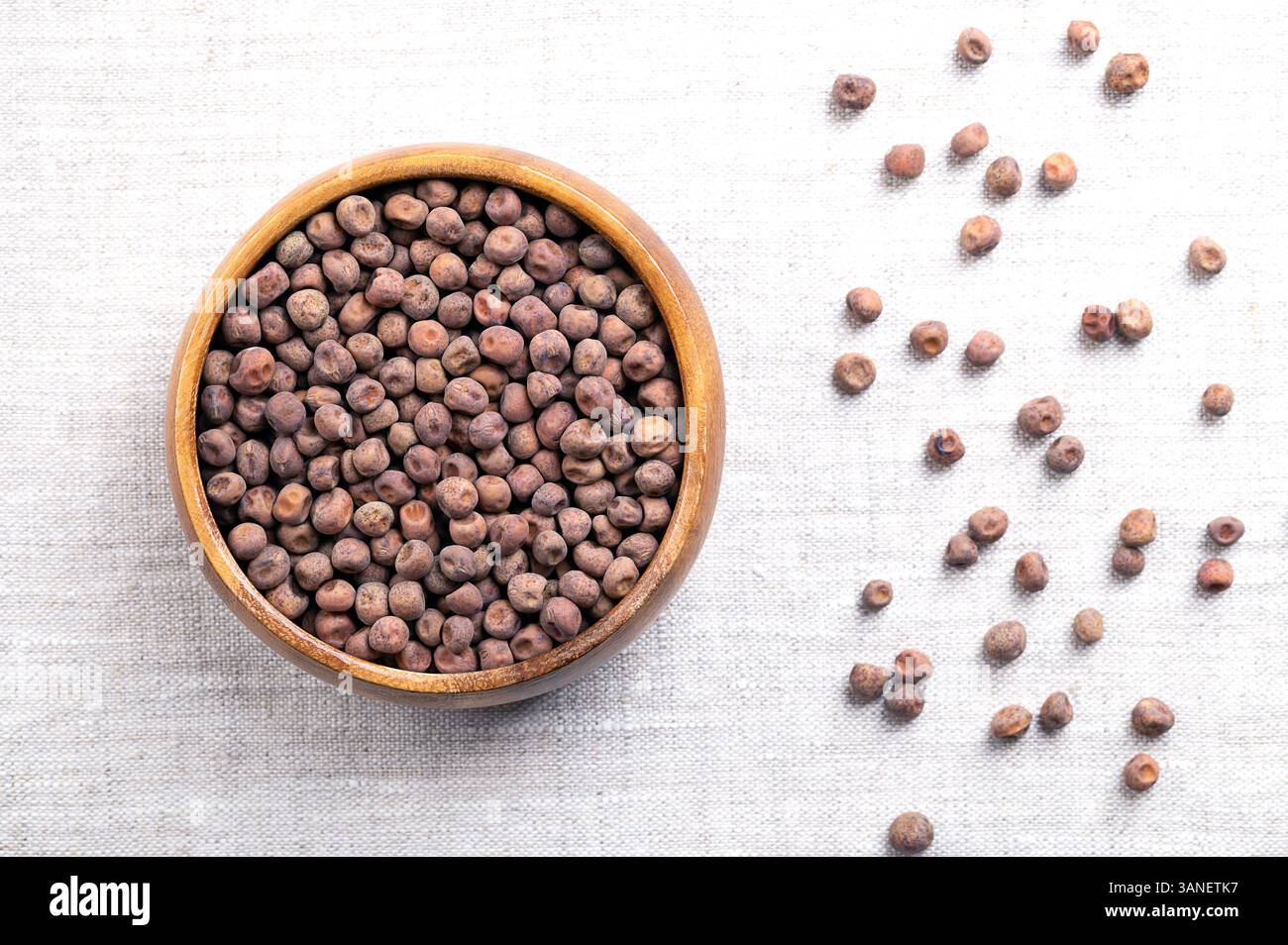Schneeerbsenkerne in einer Holzschale auf Leinen. Samen der Schneeerbsenpflanze, einer essbaren Schotenerbse, auch bekannt als Chinesische Erbsenschoten. Getrocknete, braune, reife Früchte. Stockfoto