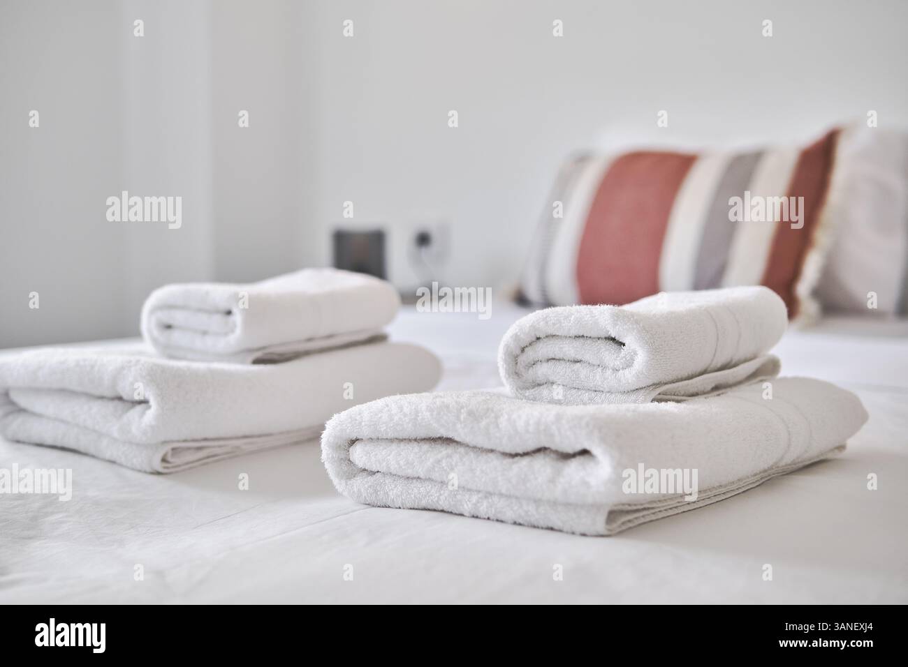 Nahaufnahme von frisch gefalteten weißen Handtüchern, die in einem modernen, minimalistischen Schlafzimmer auf einem ordentlich gefertigten Bett liegen Stockfoto