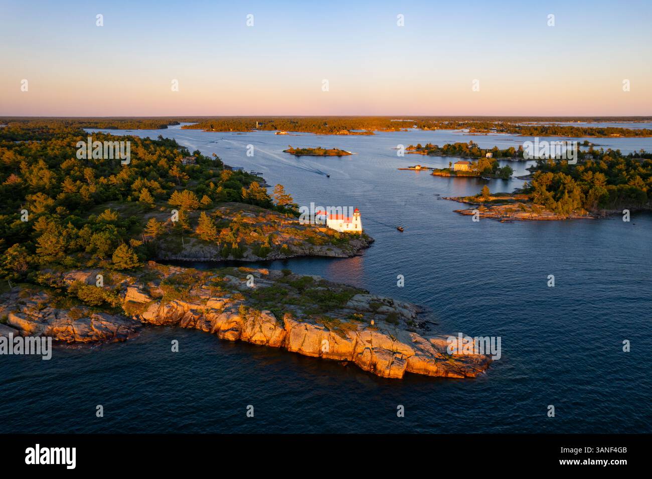 Blick aus der Vogelperspektive auf den Leuchtturm Pointe au Baril, Inseln und Wald mit felsiger Küste bei Sonnenuntergang, Georgian Bay, Kanada. Stockfoto