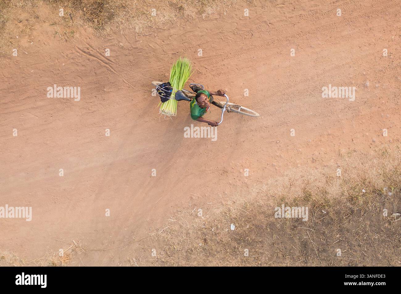 Western Area, Sierra Leone - 28. Dezember 2020: Aus der Vogelperspektive eines Afrikaners, der auf unbefestigter Straße auf einem Fahrrad im Western Rural Area, Sierra Leone, fährt. Stockfoto