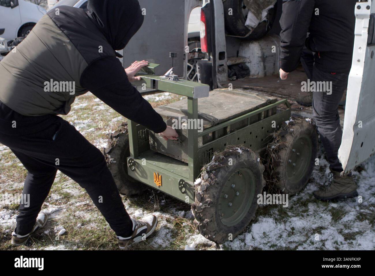 Ein Mann hält sich am Griff eines Containers fest, der auf einen bodengebundenen Roboterkomplex geladen wurde, während der umfangreichsten Versuche der Ukraine mit Bodenrobotern, die vom Brave1 Cluster in der Region Kiew, Ukraine, am 11. April 2025 durchgeführt wurden. Die Tests konzentrierten sich auf Fernkommunikation, Belastbarkeit und Widerstand gegen elektronische Kriegsführung. (Foto: Eugen Kotenko/Ukrinform) Stockfoto