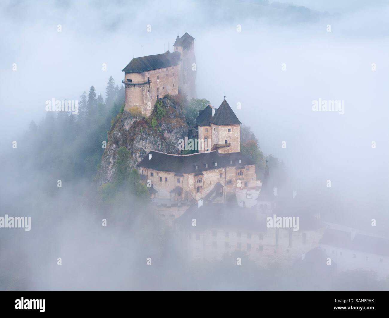 Blick aus der Vogelperspektive auf die Burg Orava, die bei Sonnenaufgang im Nebel liegt, mit umliegenden Bergen und Bäumen, Oravsky Podzamok, Zilina, Slowakei. Stockfoto