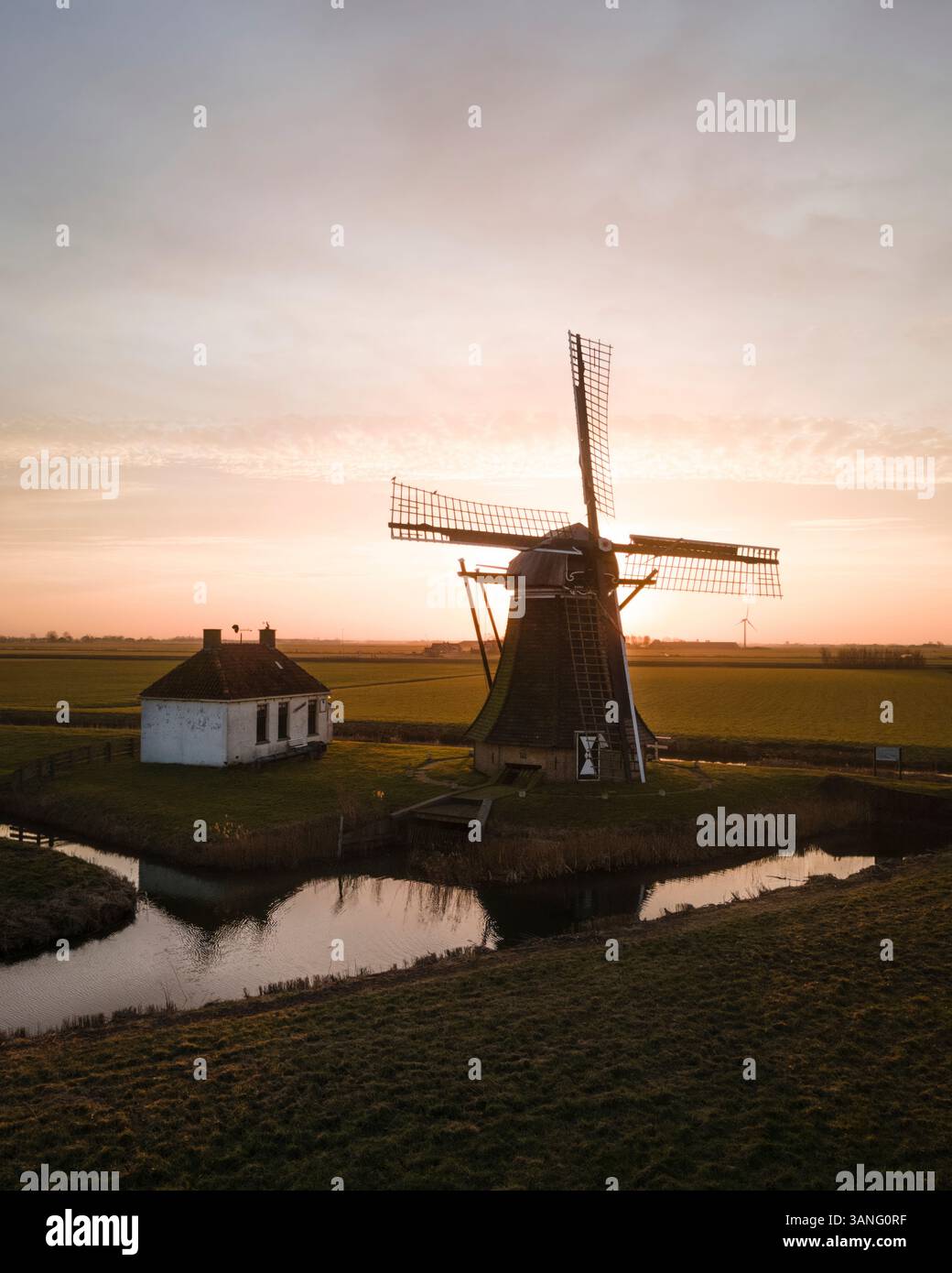 Aus der Vogelperspektive auf eine malerische Windmühle bei Sonnenaufgang mit ruhigen Reflexen auf dem Wasser, Tjerkwerd, Niederlande. Stockfoto