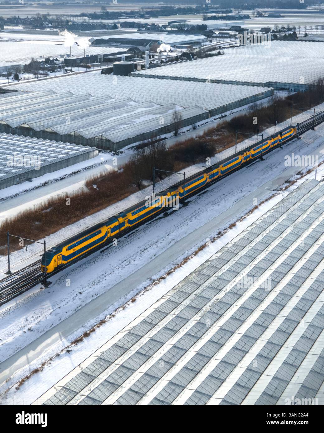 Luftaufnahme von schneebedeckten Gewächshäusern und einem Zug auf einer Eisenbahnstrecke, Heerhugowaard, Niederlande. Stockfoto