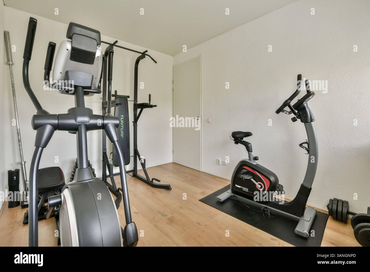 Mit verschiedenen Fitnessgeräten, die in einem eleganten, minimalistischen Home-Gym-Ambiente mit Holzfußboden und neutralen Wänden angeordnet sind. Stockfoto