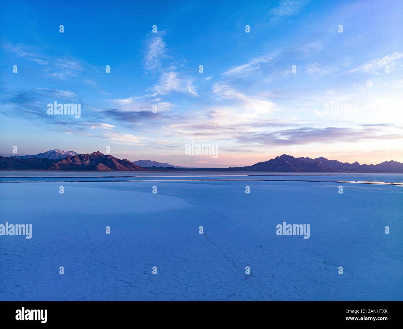 Blick aus der Vogelperspektive auf die atemberaubenden Bonneville Salt Flats bei einem ruhigen Sonnenuntergang mit weiten Bergen und heiterem Himmel, Wendover, Utah, USA. Stockfoto