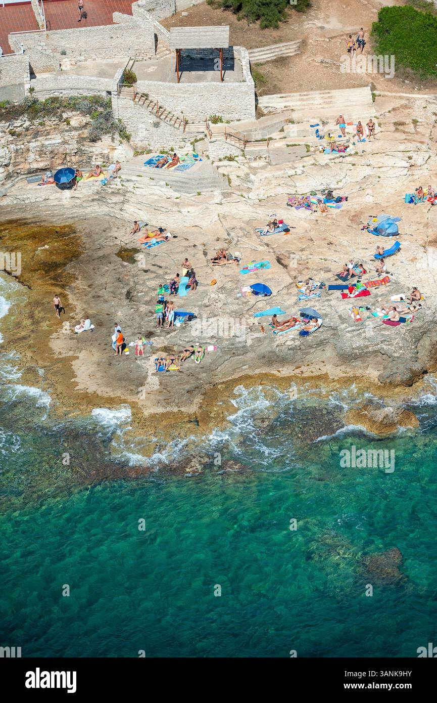 Blick aus der Vogelperspektive auf einen malerischen Strand mit Sonnenbaden an Sandstränden und felsigen Felsvorsprüngen, Pula, Istrien, Kroatien. Stockfoto