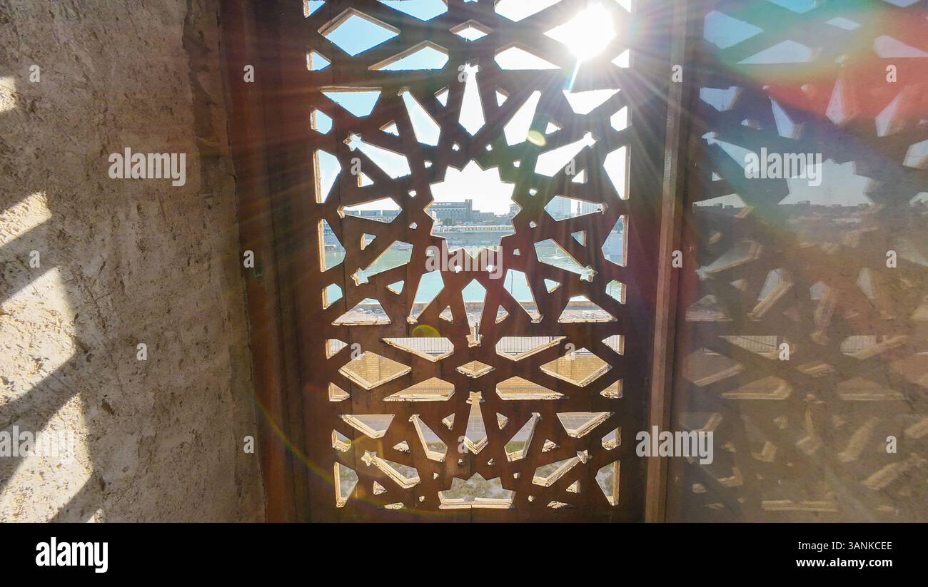Sonnenlicht strömt durch ein kompliziertes Gitterfenster und wirft geometrische Schatten. Stockfoto
