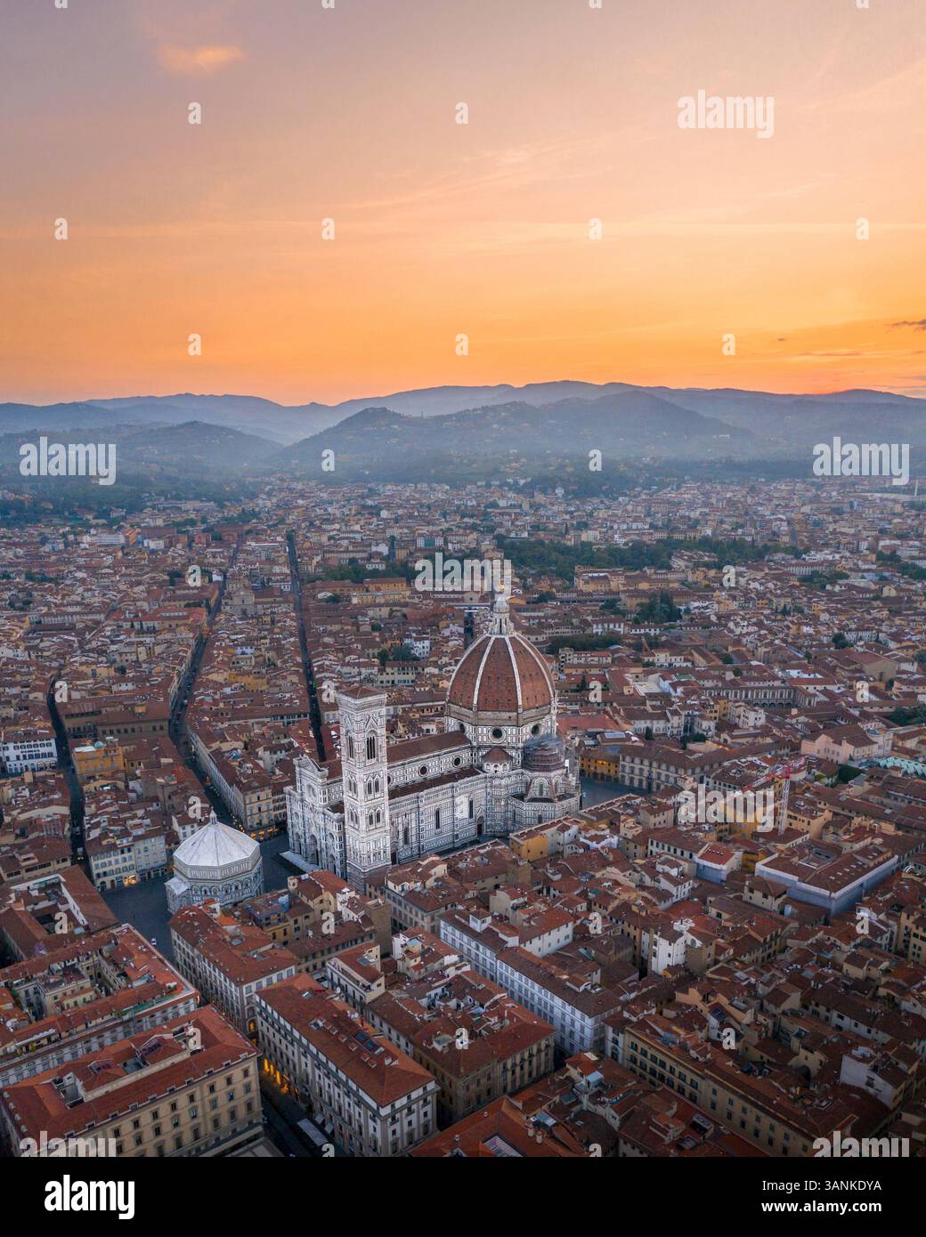 Blick aus der Vogelperspektive auf die wunderschöne Stadtlandschaft mit der berühmten Kathedrale und mittelalterlichen Türmen unter einem orangen Himmel bei Sonnenuntergang, Florenz, Italien. Stockfoto