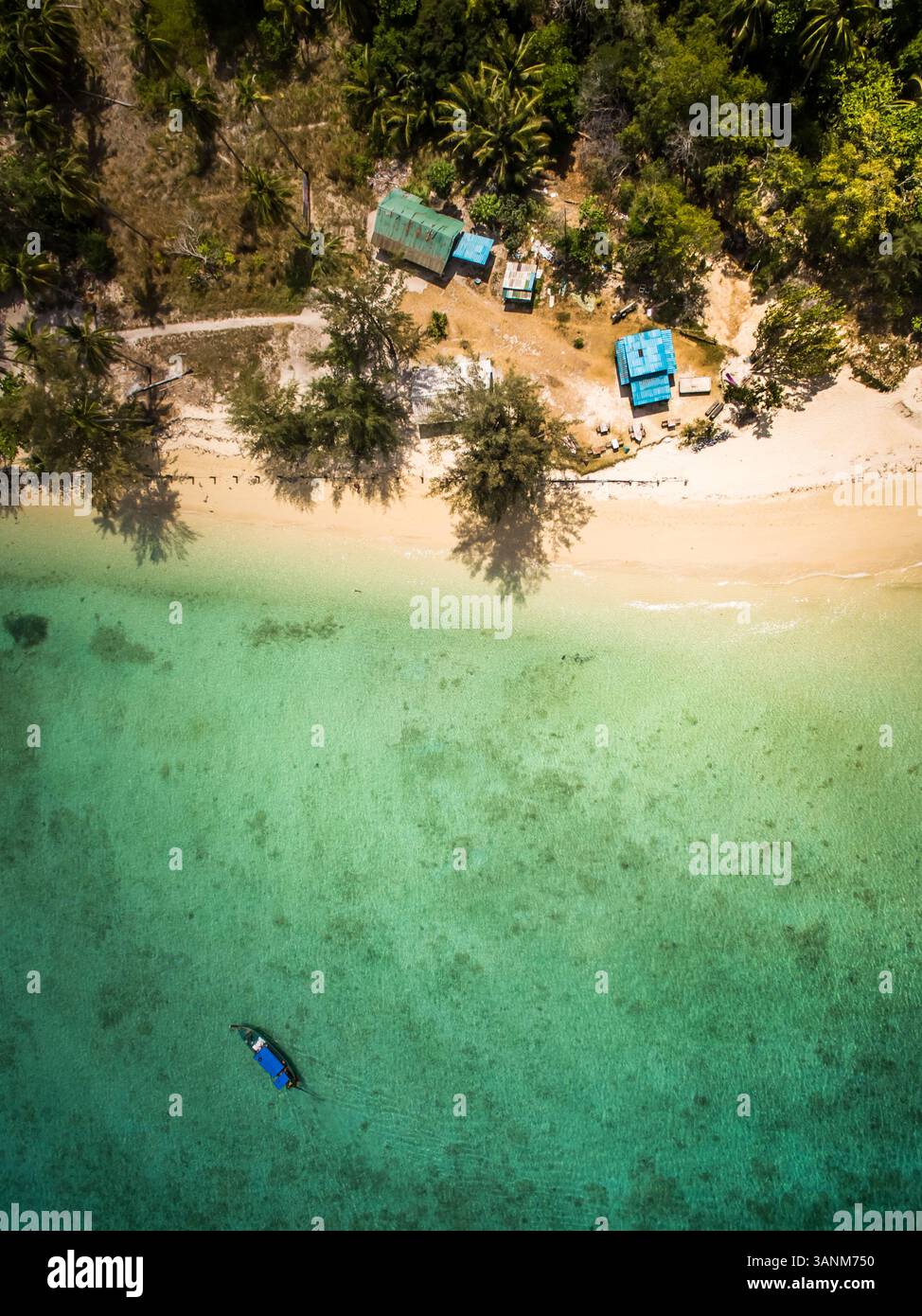 Aus der Vogelperspektive eines Bootes, das im paradiesischen Meer in der Nähe von kleinen Häusern am Strand im Chao Mai Nationalpark in Thailand verankert ist. Stockfoto