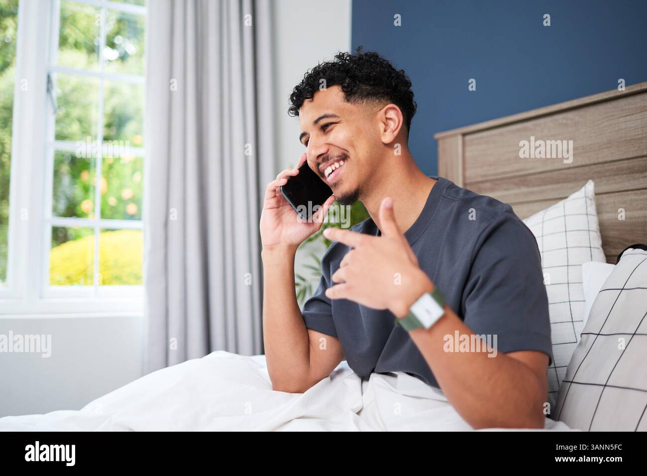 Lächelnder junger Mann im Bett, der ein angenehmes Telefongespräch führt Stockfoto