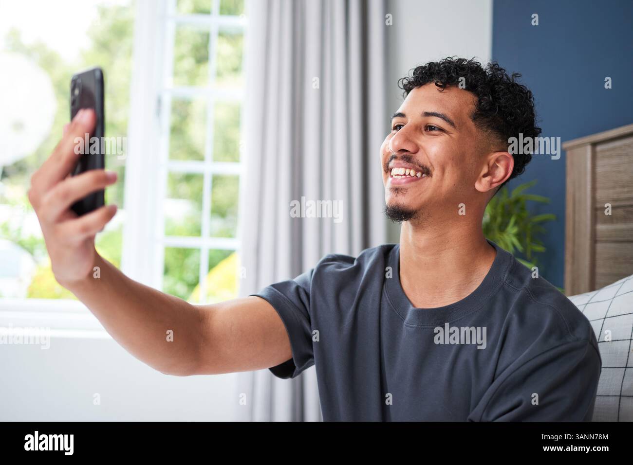 Lächelnder junger Mann, der ein Smartphone hält und zu Hause ein Selfie macht Stockfoto
