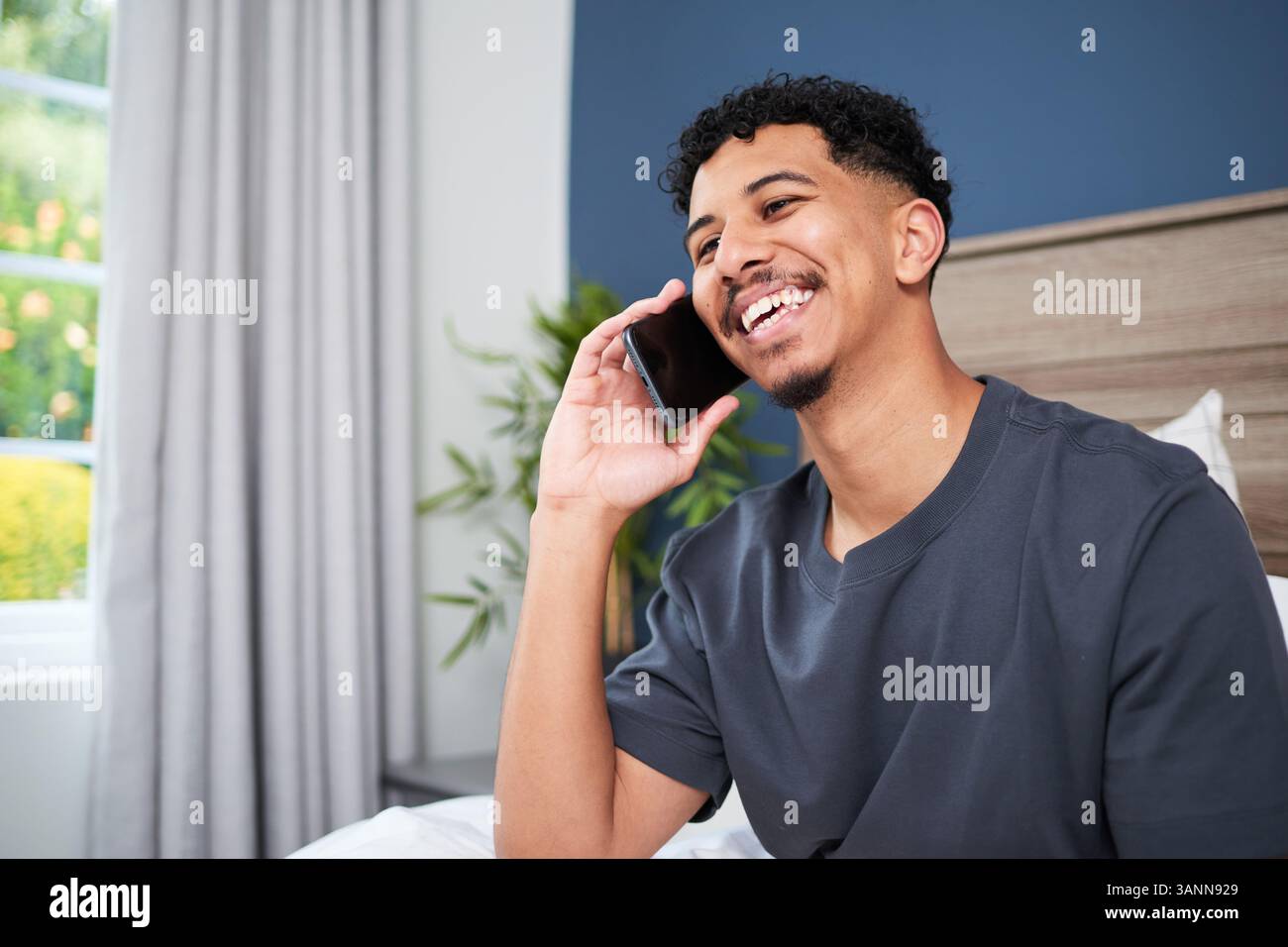 Lächelnder junger Mann, der zu Hause in komfortabler Umgebung einen entspannten Telefonanruf genießt Stockfoto