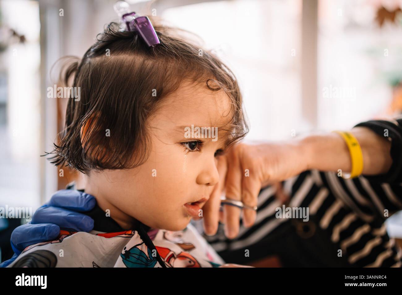Das Baby bekommt den ersten Haarschnitt. Friseur schneidet Haare von Baby latino hispanic Mädchen in einem Friseursalon Stockfoto