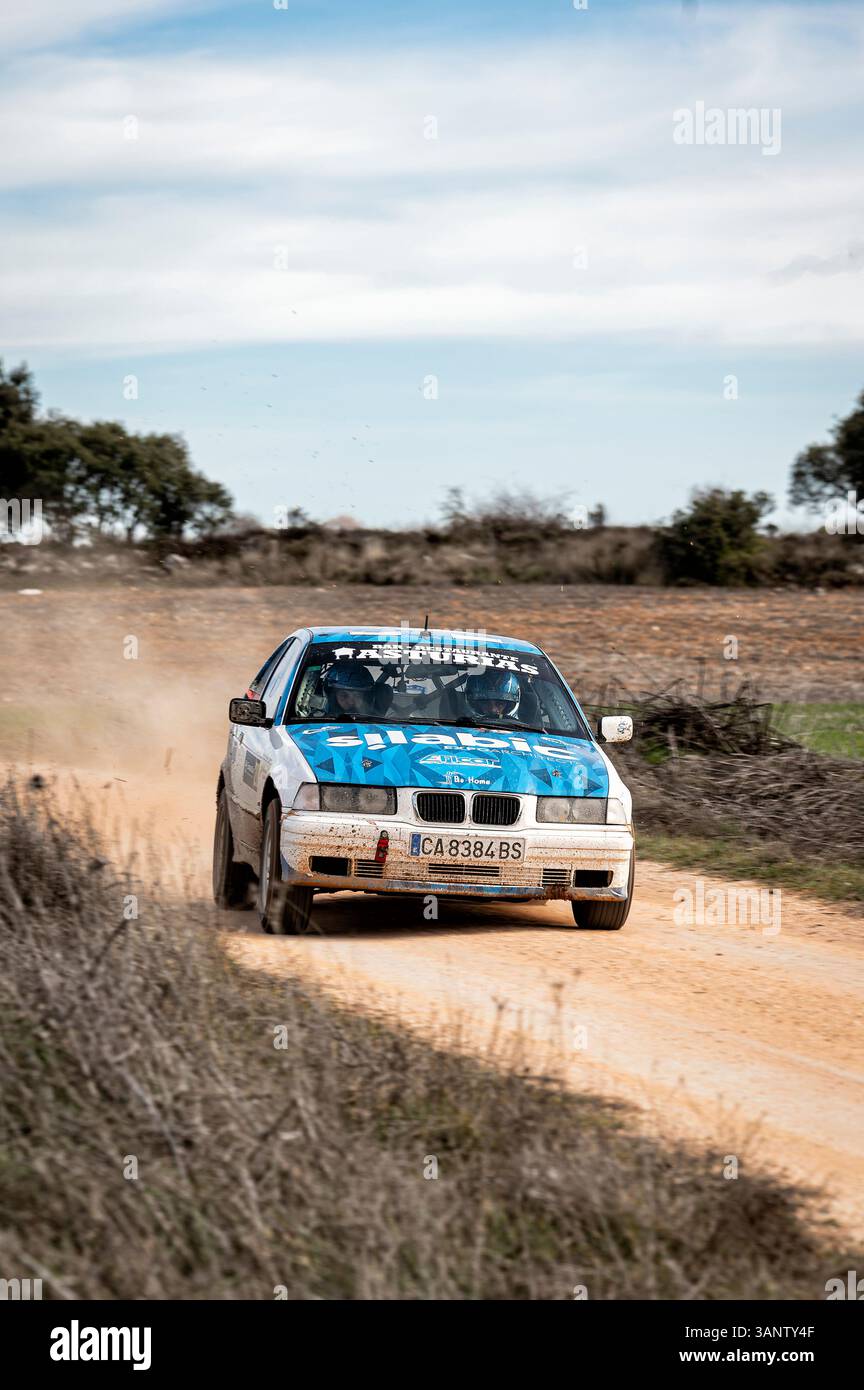 Madrid, Spanien; 15.02.2025: Ein blau-weißer BMW 323i E36 fährt auf einer Kies-Rallye-Strecke und schleudert Staub, während er durch die Landschaft fährt. Die Co- Stockfoto