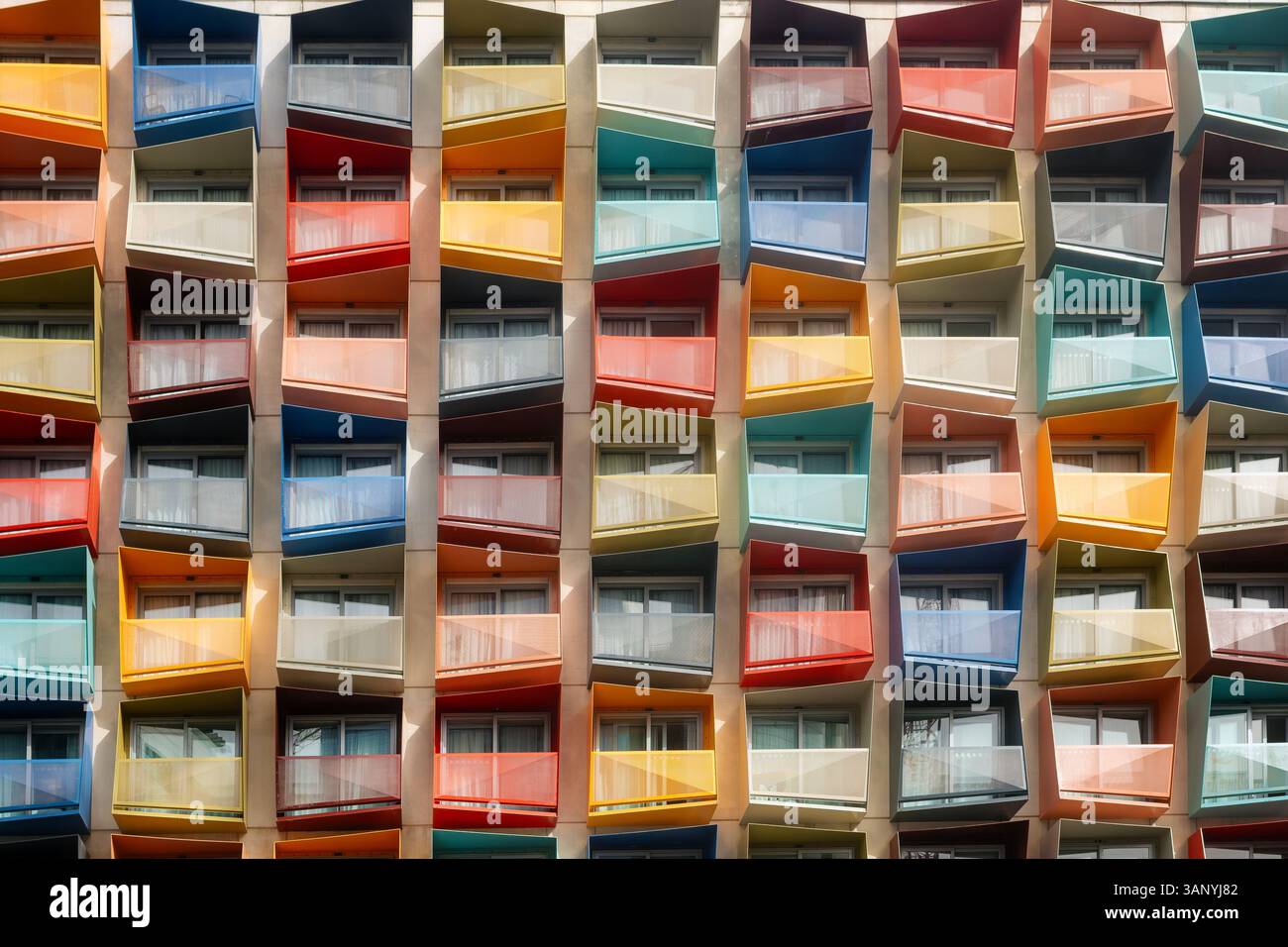 Helles, modernes Apartmentgebäude mit farbenfrohen eckigen Balkonen in einem rhythmischen, symmetrischen Muster. Ideal für städtisches, architektonisches oder abstraktes Design Stockfoto